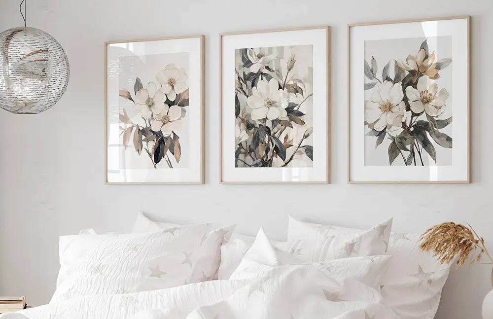 Floral art prints trio in soft beige and grey tones styled above white bedhead