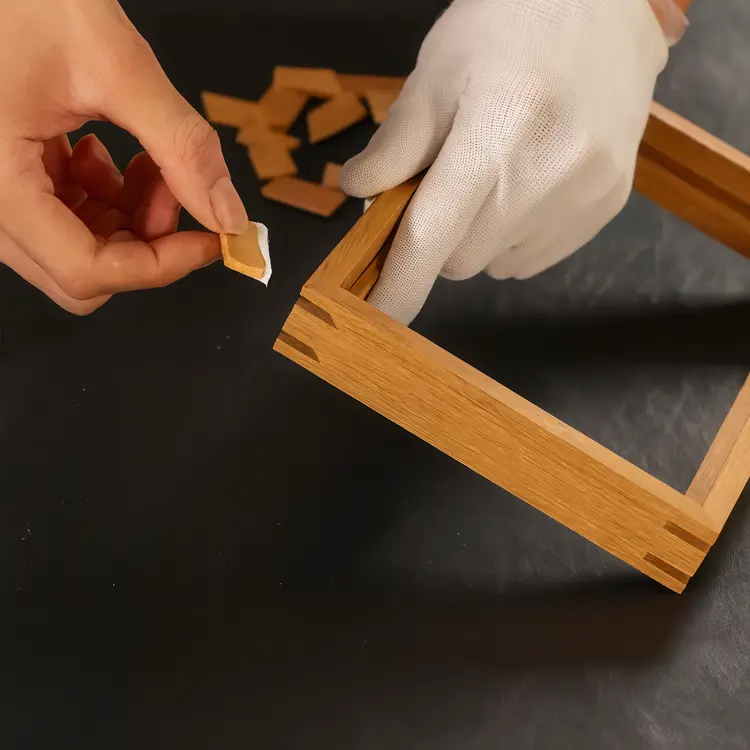 Hand assembling wooden photo frame corner showing precise joinery craftsmanship