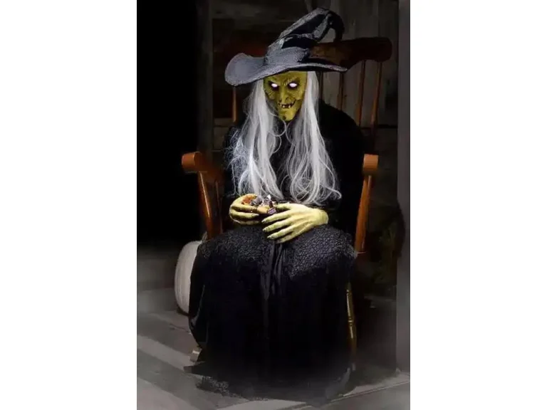 Life-size witch halloween decoration with glowing eyes and long white hair sitting on rocking chair.