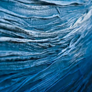 Macro close-up of deep, wave-like blue mixed media texture showing intricate ridges and valleys.