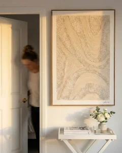 Large neutral-toned textured painting hanging in a minimalist hallway under soft, indirect natural light