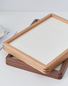 A stack of premium solid timber frames by VeeArt, showing natural light wood and dark walnut finishes with quality joinery, contrasting with MDF frames.