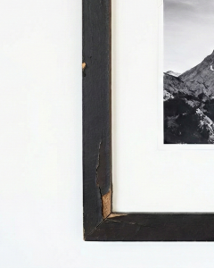 Close-up detail of a damaged cheap frame corner, showing the black veneer foil peeling away to reveal the fibrous MDF particleboard underneath.