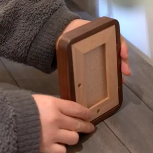Hand holding a Veeart walnut solid wood picture frame, displaying the matching walnut backboard.