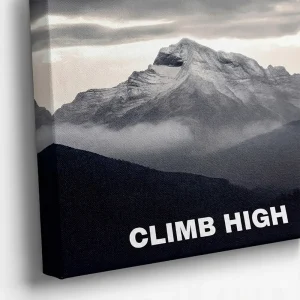 Close-up view of a black and white canvas print showing a rugged mountain peak surrounded by clouds with the white text "CLIMB HIGH" at the bottom right, highlighting the textured canvas material.