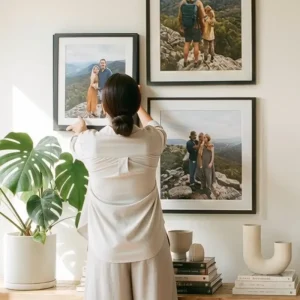 Woman hanging multiple black framed wall art pieces on a gallery wall