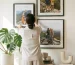 Woman hanging multiple black framed wall art pieces on a gallery wall