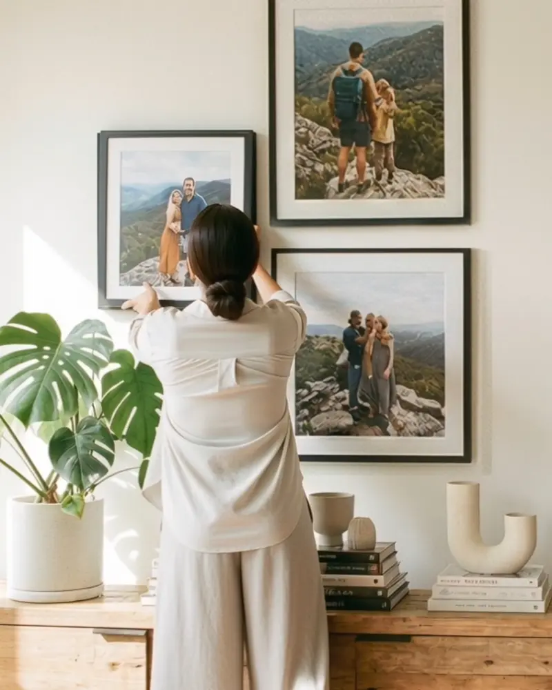 Woman hanging multiple black framed wall art pieces on a gallery wall